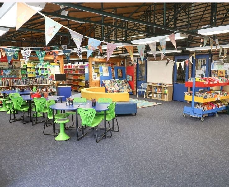 School library with tables and chairs, shelves of books and colourful banners