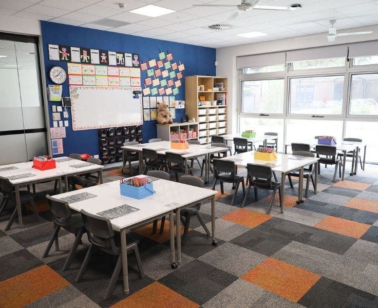 Classroom with tables and chairs, checked carpet, whiteboard and cupboards