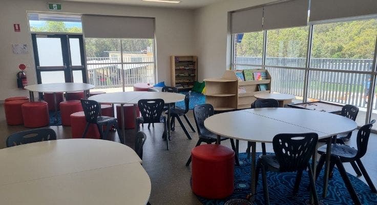 OOSH room with tables and chairs, bookshelf and reading corner with carpet and cushions
