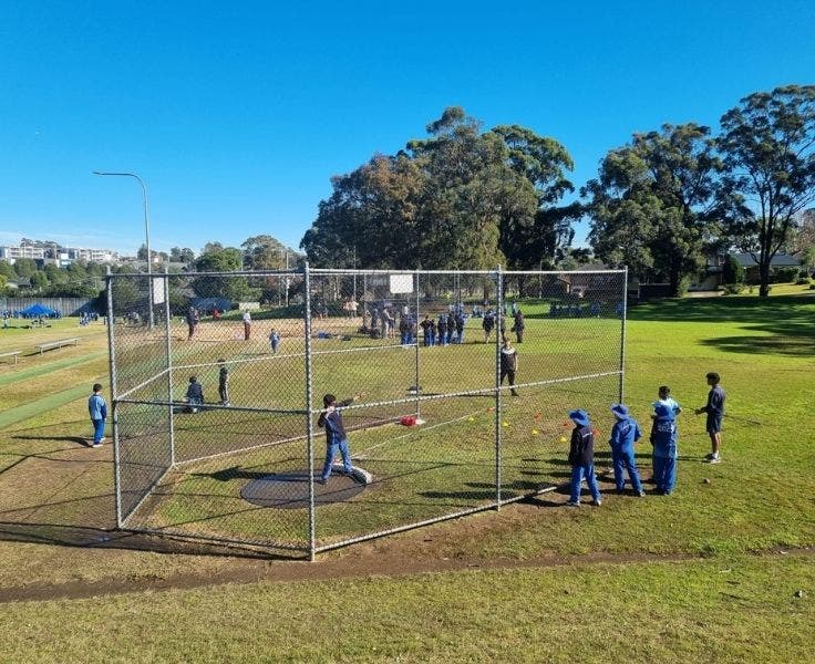 Student at a sports field preparing to throw a shot put while other students and teachers look on