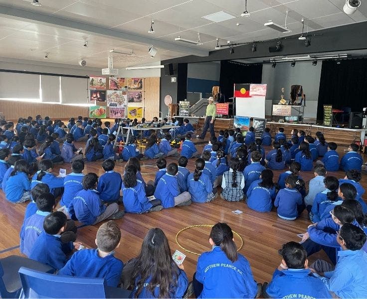 students sitting in a school hall listening to a man speaking